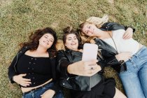 Amigos deitados na grama, tirando uma selfie — Fotografia de Stock