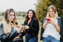 Tre giovani donne che usano i loro telefoni nel parco — Foto stock