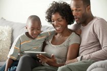 Niño con los padres en el sofá usando tableta digital - foto de stock