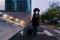 Mujer de negocios caminando con maleta, usando mascarilla - foto de stock
