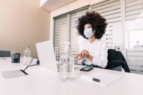 Empresária vestindo máscara facial e usando higienizador de mãos — Fotografia de Stock