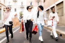 Four female friends walking along street with shopping bags — Stock Photo