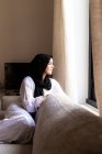 Young muslim woman looking through window at home — Stock Photo