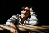 Ragazzo adolescente seduto a tavola in interni scuri con luce solare — Foto stock