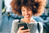 Молодая женщина смотрит на телефон на улице, улыбаясь — стоковое фото