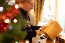Мужчина упаковывает посылки на Рождество дома — стоковое фото