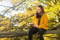 Woman sketching, sitting on tree branch — Stock Photo