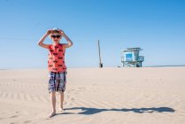 Boy on sunny sandy beach, wearing sunglasses and hat — Stock Photo