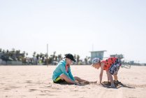 Hermana y hermano jugando en la arena en la playa - foto de stock