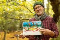 Reino Unido, Londres, Epping Forest, Hombre mostrando su pintura en el paisaje de otoño - foto de stock