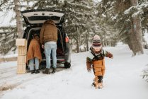 Канада, Онтаріо, дівчинка (2-3) йде в снігу і батьки розпаковують автомобільний багажник — стокове фото