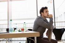 Germany, Bavaria, Munich, Young man sitting on chair by desk and thinking — Stock Photo