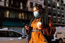 Italien: Frau mit Mundschutz hält Smartphone und Einwegbecher auf der Straße — Stockfoto