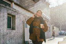 Италия, улыбающаяся женщина разговаривает по телефону и держит одноразовую чашку на городской улице — стоковое фото