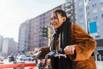 Italia, Mujer joven sonriente con bicicleta en la calle de la ciudad - foto de stock