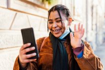 Італія, молода жінка з масками обличчя посміхається і розмахує до смартфона — стокове фото