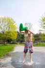 Канада, Кингстон, Мальчик без рубашки льет воду из резинового ботинка на голову — стоковое фото