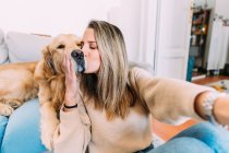Italy, Young woman kissing dog at home — Stock Photo
