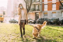 Italy, Young woman and dog walking on grass — Stock Photo