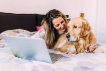 Italien: Junge Frau mit Hund im Bett schaut auf Laptop — Stockfoto