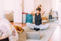 Italy, Young woman stretching in front of laptop on floor — Stock Photo