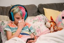 Canadá, Ontario, Niño con el pelo colorido y auriculares que soplan la nariz en el sofá - foto de stock