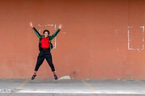 Italia, Toscana, Pistoia, Mujer sonriente saltando contra la pared - foto de stock