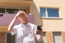 Germany, Cologne, Albino man in white shirt holding smart phone — Stock Photo