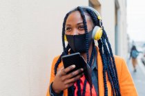 Италия, Милан, модная женщина с маской для лица, наушниками и смартфоном — стоковое фото