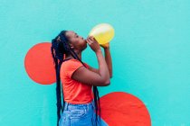 Italy, Milan, Young woman with braids blowing yellow balloon — Stock Photo