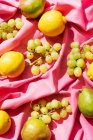 Вид зверху на лимони, груші та виноград на рожевій тканині столу — стокове фото