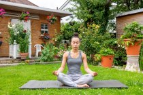 Großbritannien, London, Frau meditiert auf Rasen vor Haus — Stockfoto