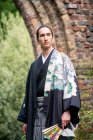 Великобритания, портрет молодого человека в кимоно, держащего веер в парке — стоковое фото