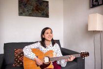 Smiling woman playing acoustic guitar in living room — Stock Photo