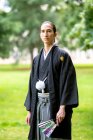 Великобритания, портрет молодого человека в кимоно, держащего веер в парке — стоковое фото