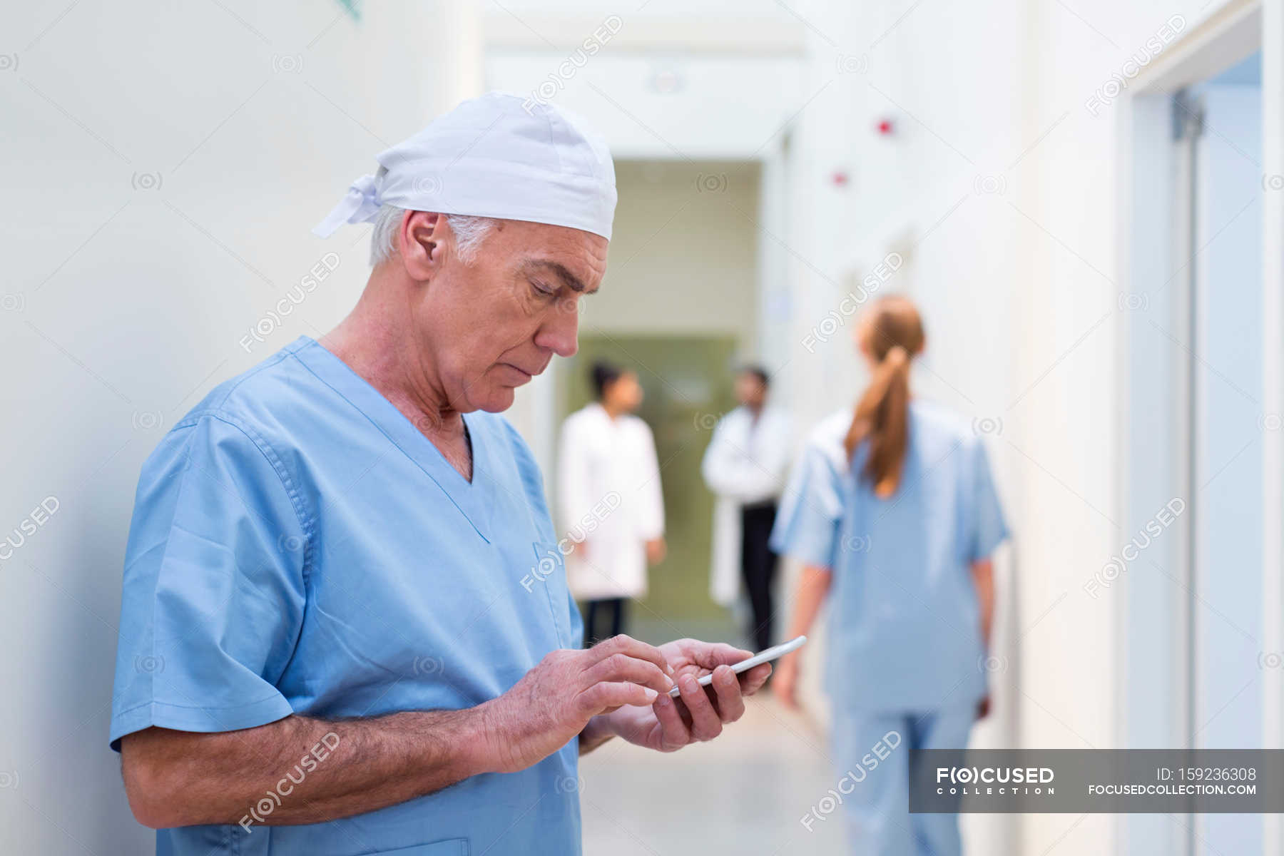 Doctor in hospital looking at mobile phone — four people, skill - Stock  Photo | #159236308