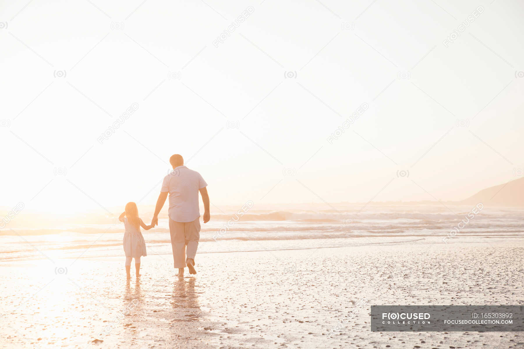 Father and daughter holding hands paddling in ocean — ankle Deep In