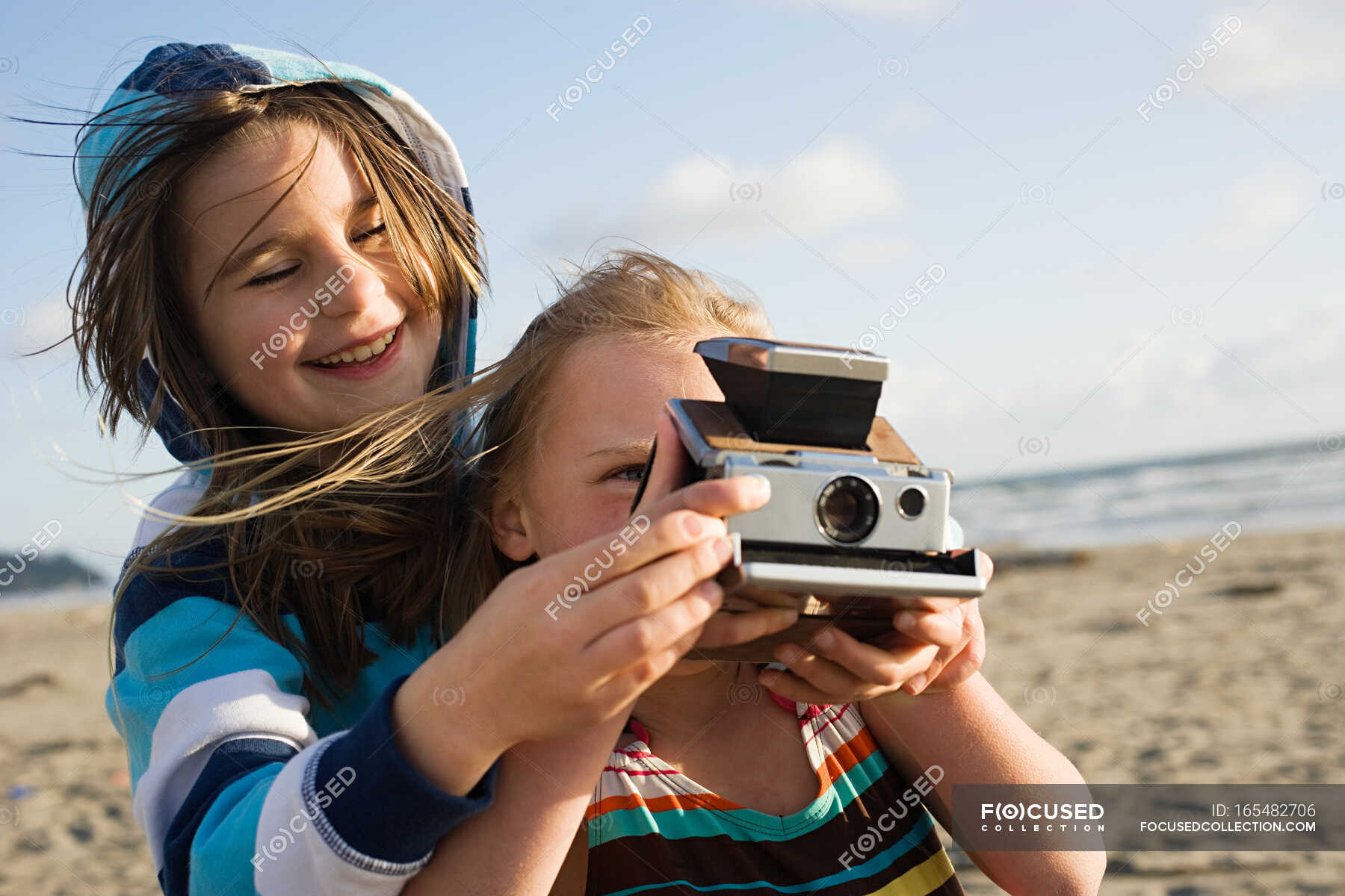Girl showing friend how to use instant camera at beach — only children