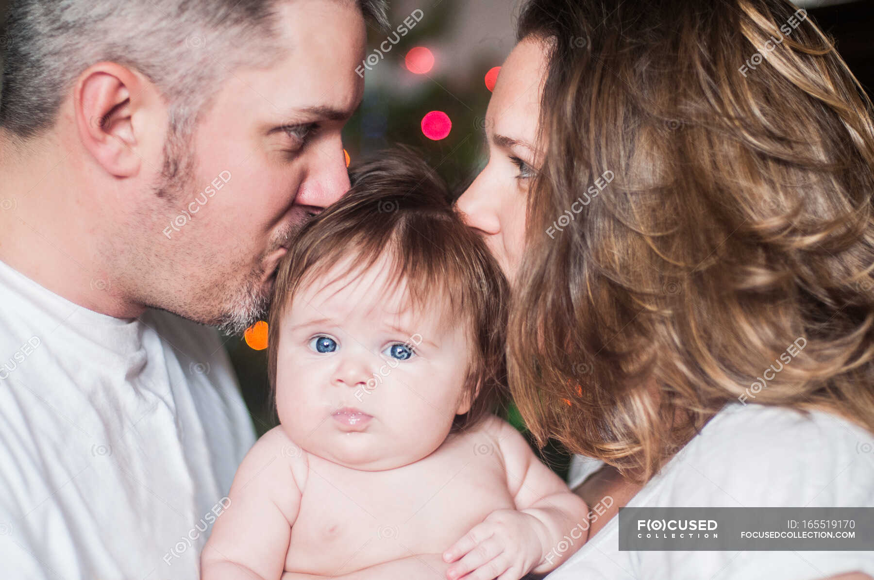 Mother and father face to face holding baby girl, kissing on head — family life, bonding Stock
