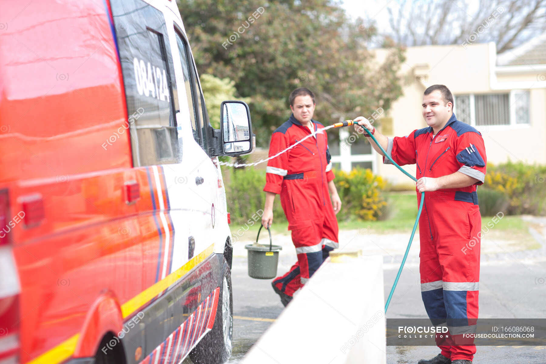Paramedics cleaning ambulance with hosepipe — Front View, emergency