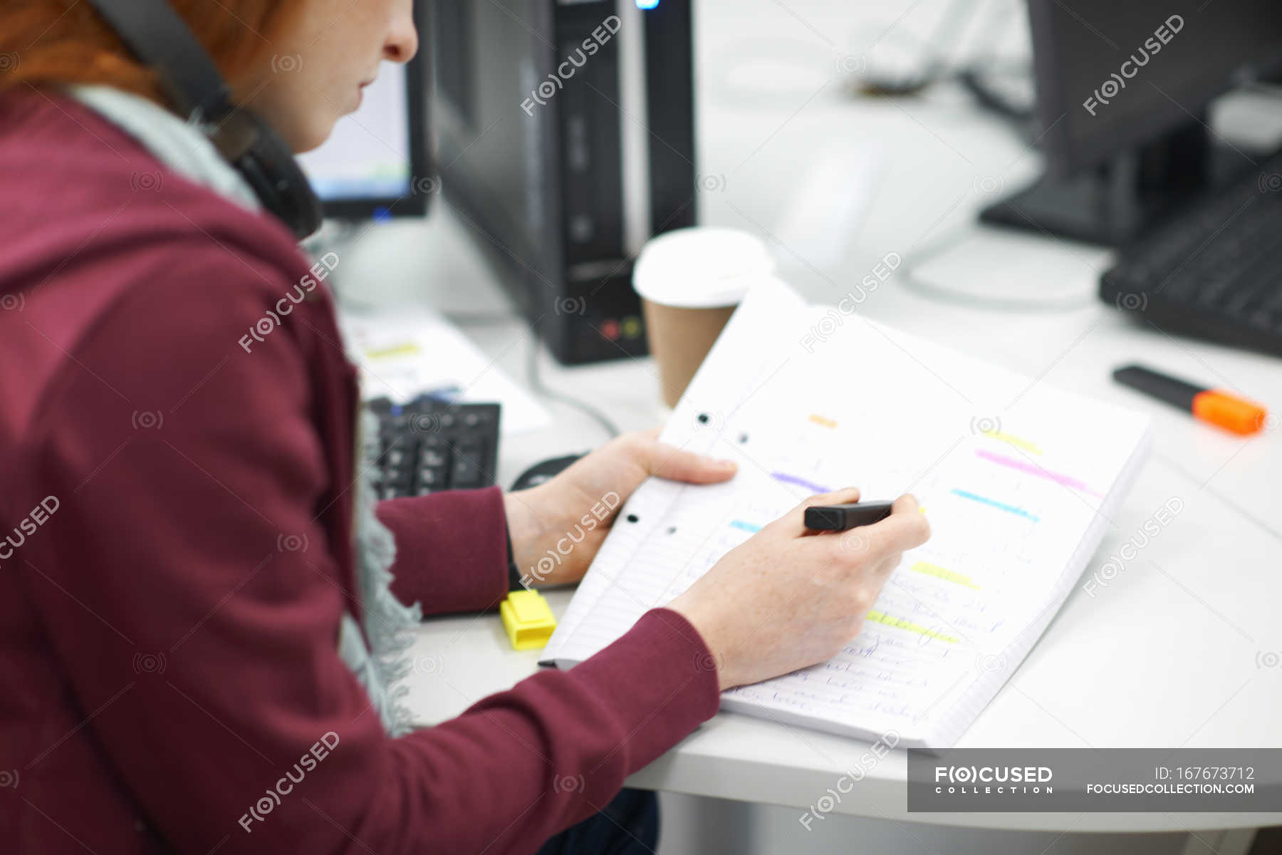 Young Female College Student At Computer Desk Writing In Notebook