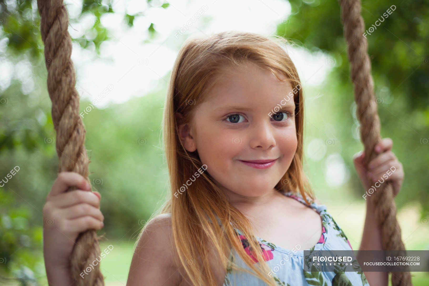 Smiling girl sitting in tree swing, focus on foreground — childhood ...