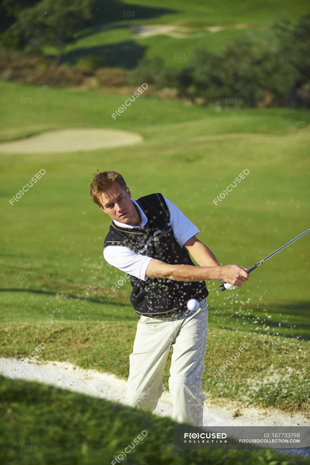 Golfer taking golf swing in sand trap, golf ball in mid air — man ...