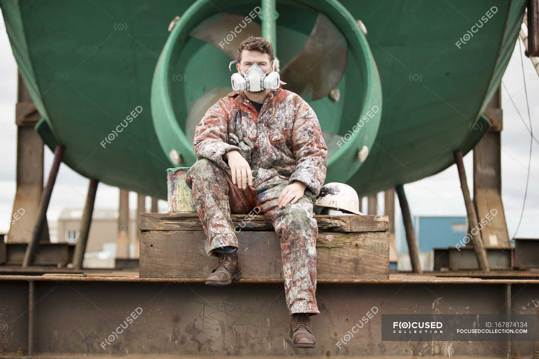 Portrait of male ship painter wearing protective mask in front of green ...