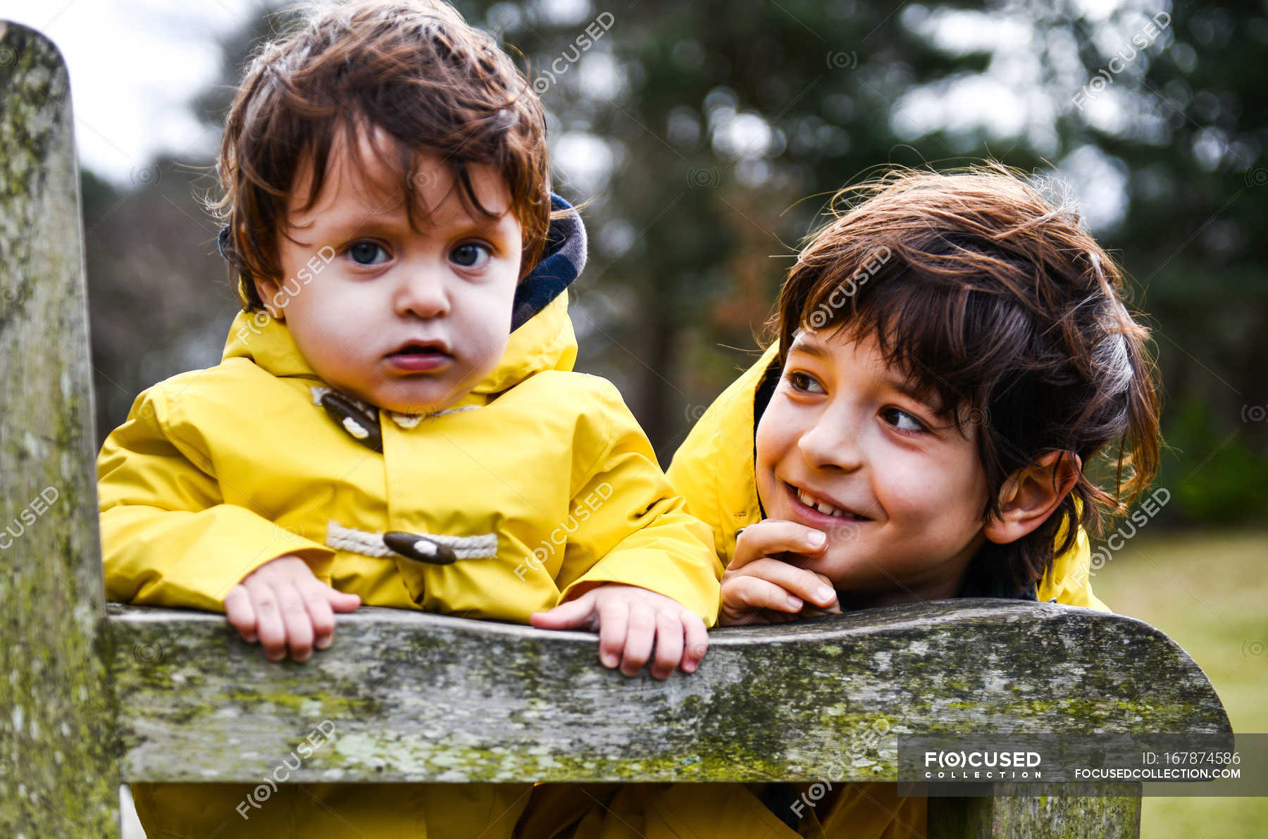 portrait-of-baby-boy-and-big-brother-in-yellow-anoraks-on-park-bench