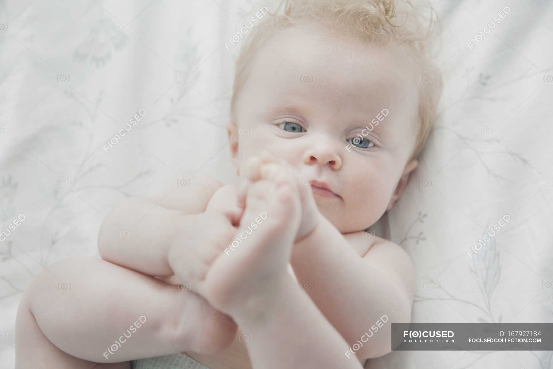 baby-girl-lying-on-back-holding-feet-concentration-female-stock