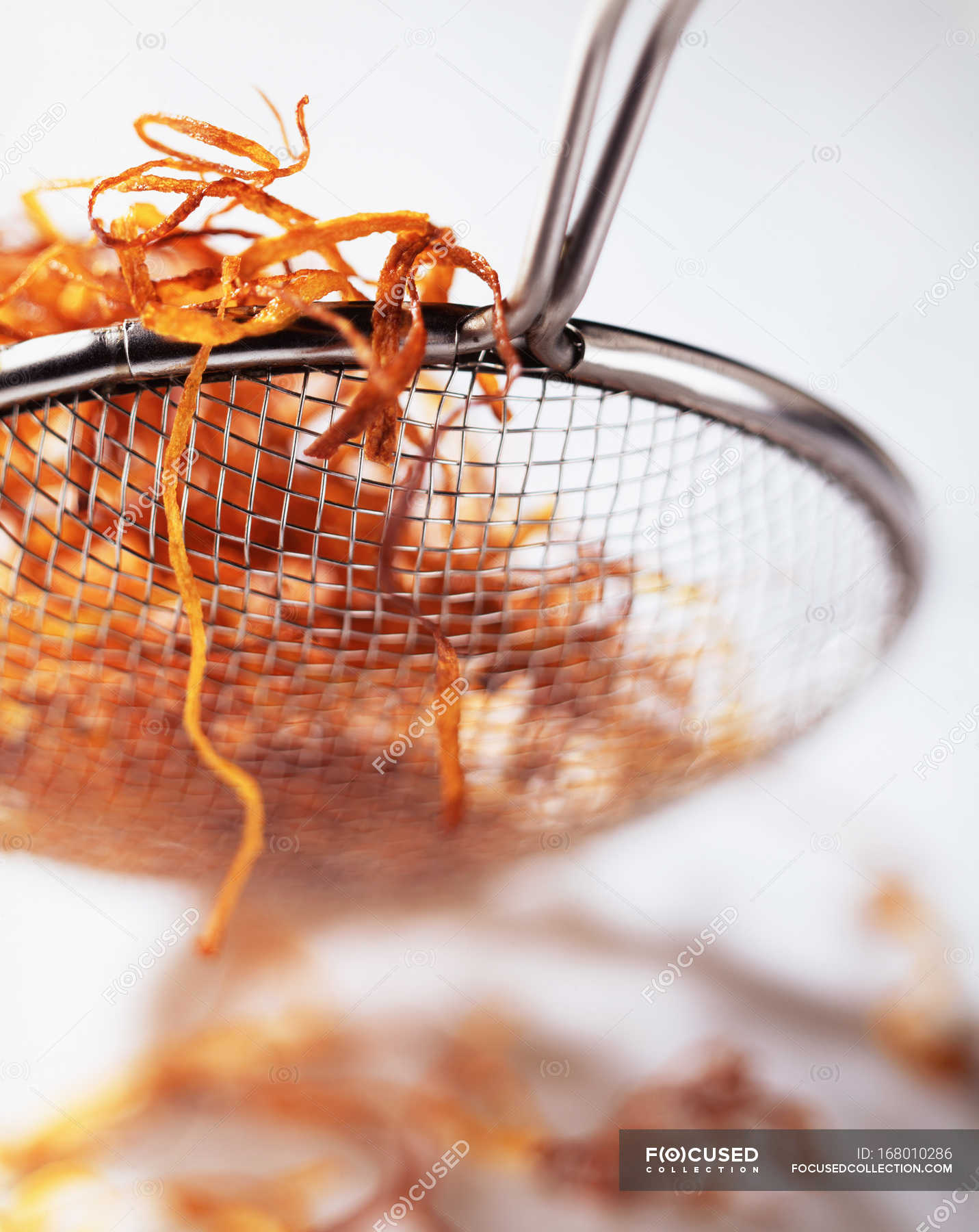 Deep fried carrot slices in sieve, close up shot — white background