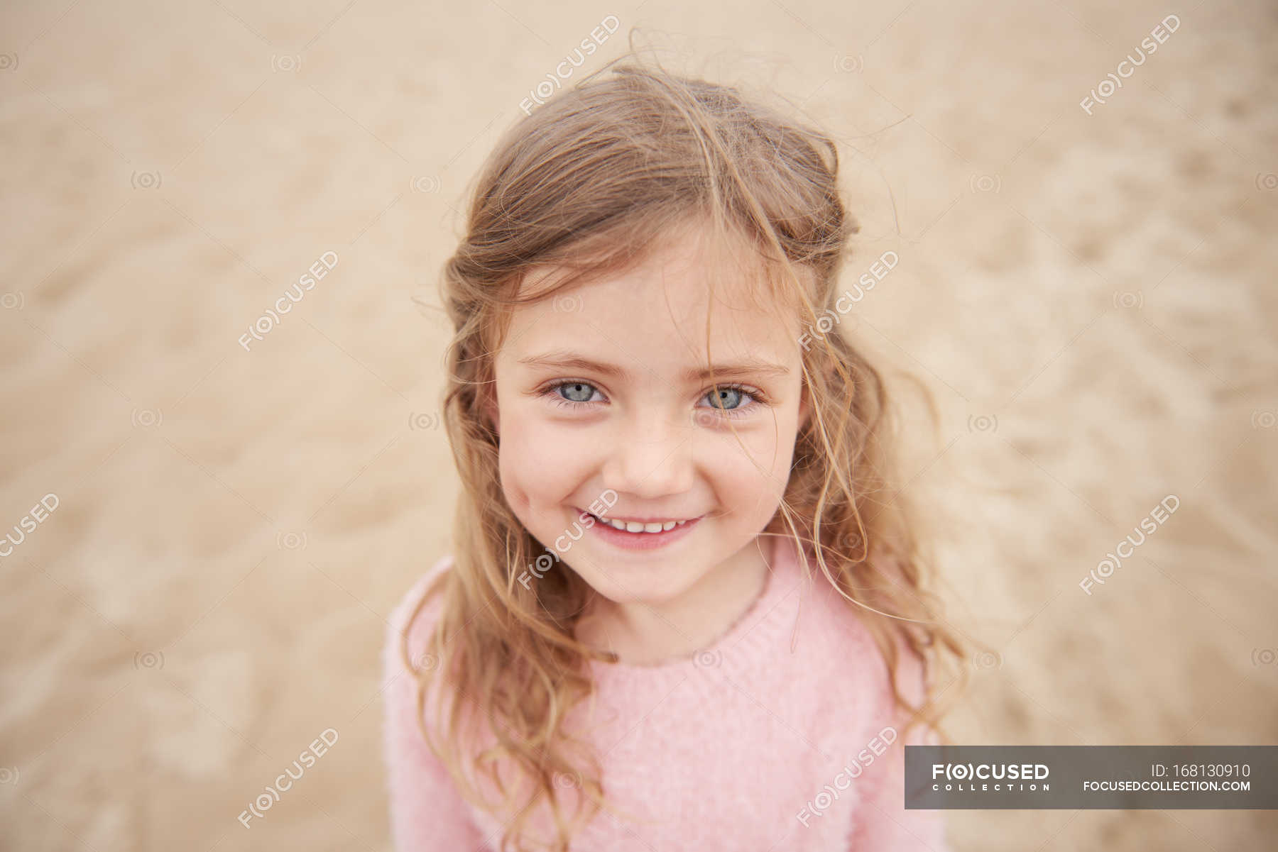 little-girl-smiling-on-beach-against-sand-head-and-shoulders-only