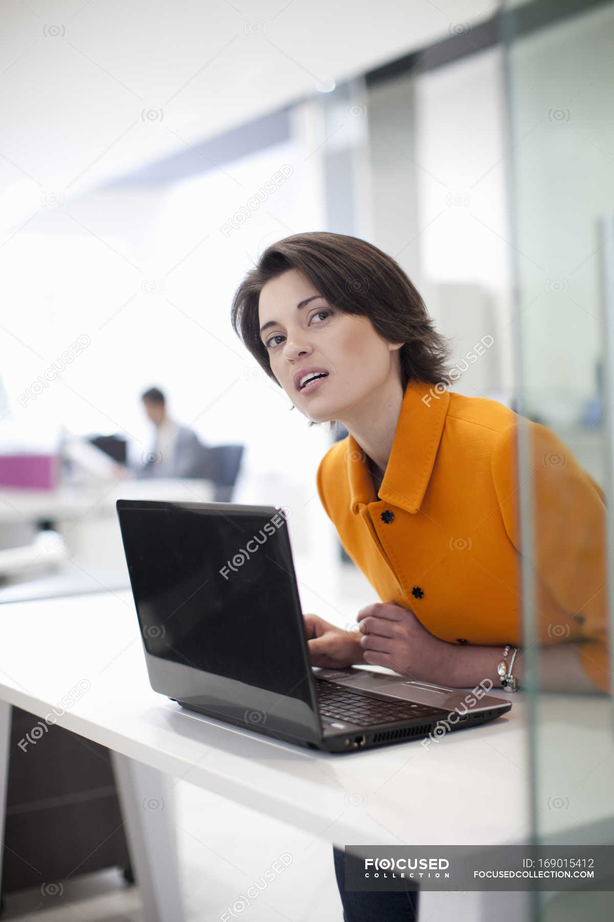 Female office worker using laptop, leaning forward — orange color, brunette  - Stock Photo | #169015412