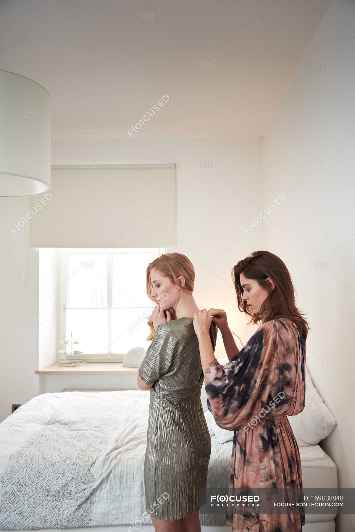 Two Young Women Getting Ready In Bedroom Zipping Dresses — Female